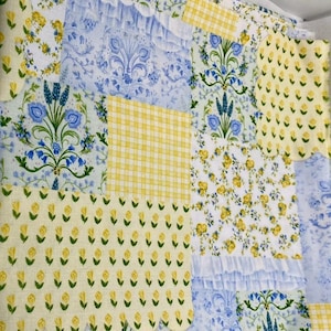 May include: Patchwork fabric with a yellow and blue floral pattern. The fabric is made up of different squares with different patterns, including a checkered pattern, a floral pattern, and a solid color pattern.