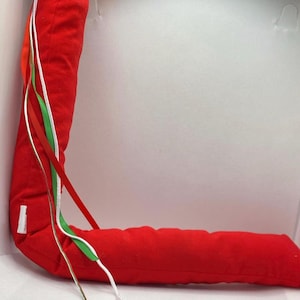 May include: A red fabric tube with white, red, and green ribbon attached. The tube is bent into a curved shape.