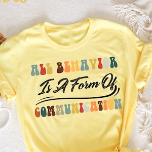 May include: Yellow t-shirt with the text "All Behavior Is A Form Of Communication" in colorful letters.