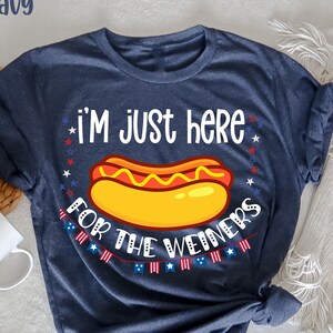 May include: A navy blue t-shirt with the text "I'm just here for the weiners" and a cartoon hot dog with mustard and ketchup. The text is surrounded by red, white, and blue stars.