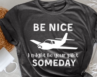 May include: Dark grey heather t-shirt with white text that reads "BE NICE I might be your pilot SOMEDAY" and a white silhouette of a small aeroplane.