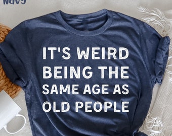 Puede incluir: Una camiseta azul marino jaspeada con el texto "It's weird being the same age as old people" impreso en blanco.