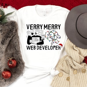 May include: White t-shirt with black text that reads "Verry Merry Web Developer" and a graphic of a person working on a computer with Christmas lights.