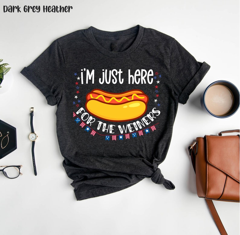 May include: Dark grey heather t-shirt with a hot dog graphic and the text "I'm just here for the weiners". The graphic includes red, white, and blue stars and a string of American flags.
