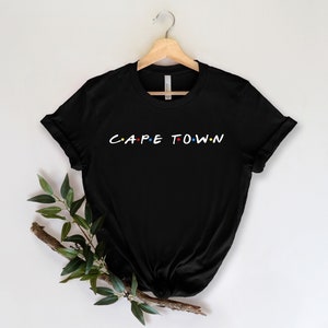 May include: Black t-shirt with a white graphic that says "C.A.P.E T.O.W.N" in the style of the "Friends" logo.