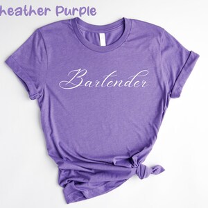 May include: A heather purple t-shirt with the word "Bartender" written in white cursive script.