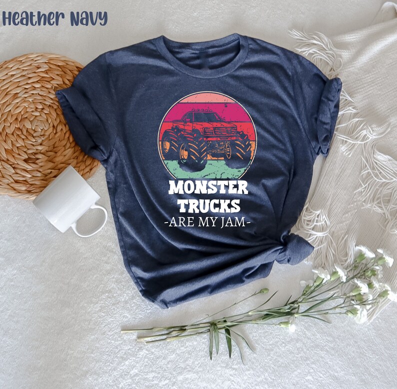 May include: Heather navy blue t-shirt featuring a vintage-style graphic of a monster truck in front of a sunset. The text "Monster Trucks - Are My Jam -" is printed below the graphic.