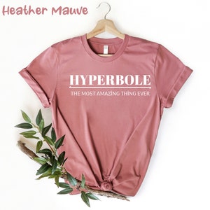 Puede incluir: Camiseta de color malva jaspeado con el texto "HYPERBOLE THE MOST AMAZING THING EVER" impreso en blanco.