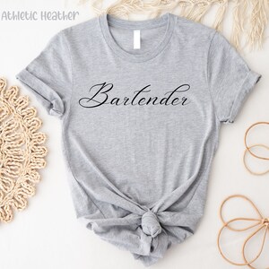 May include: A gray t-shirt with the word "Bartender" written in black cursive script.