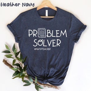 Könnte beinhalten: Heather-Marineblaues T-Shirt mit weißem Text, der "Problem Solver" lautet, und einer Taschenrechnergrafik. Der Text "#mathteacher" befindet sich unter der Grafik.