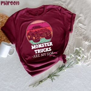 May include: A maroon t-shirt featuring a vintage-style graphic of a monster truck against a sunset backdrop. The text "Monster Trucks -Are My Jam- " is printed beneath the graphic.