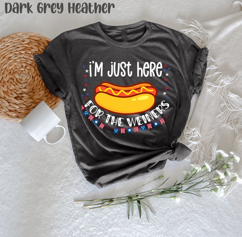 May include: Dark grey heather t-shirt with a hot dog graphic and the text "I'm just here for the weiners". The text is surrounded by red, white, and blue stars and stripes.