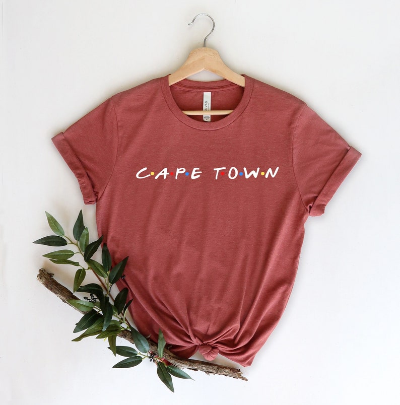 May include: A rust-colored t-shirt with the words "CAPE TOWN" in a stylized font with colorful dots.