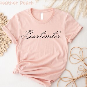 May include: A pink t-shirt with the word "Bartender" written in black cursive script.