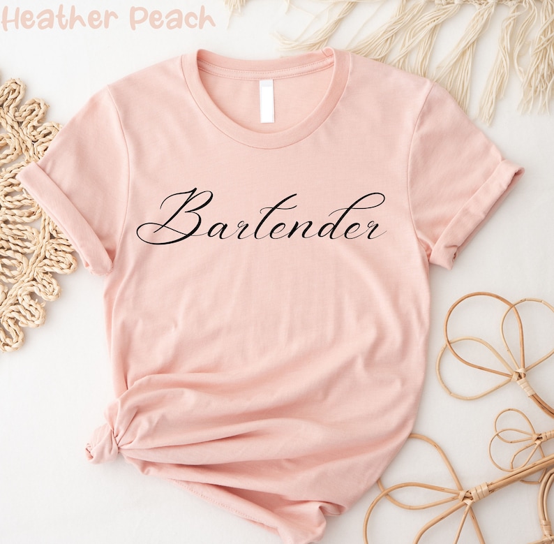 May include: A pink t-shirt with the word "Bartender" written in black cursive script.