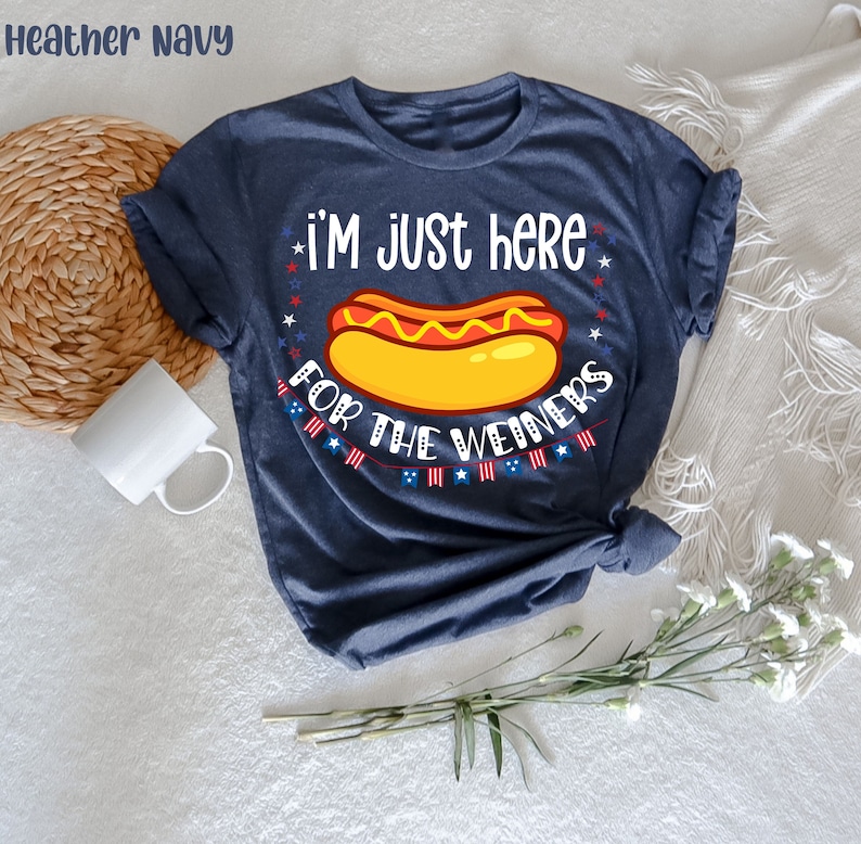 May include: A navy blue t-shirt with the text "I'm just here for the weiners" and a cartoon hot dog with mustard and ketchup. The text is surrounded by red, white, and blue stars.