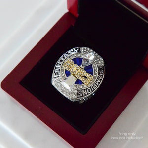 May include: A silver and gold championship ring with blue enamel and rhinestones. The ring features a football trophy design and the words "Fantasy Champions".