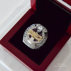 May include: A silver and gold championship ring with a purple stone and rhinestones. The ring features the words "Fantasy Champions" and a football trophy. *ring only, box not included*