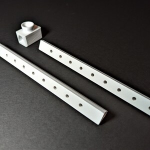May include: A set of white, rectangular furniture components with evenly spaced holes, alongside a small, white, cube-shaped piece with a cylindrical opening. The items are arranged on a dark surface.