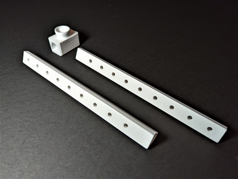 May include: A set of white, rectangular furniture components with evenly spaced holes, alongside a small, white, cube-shaped piece with a cylindrical opening. The items are arranged on a dark surface.