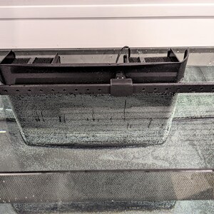 May include: A black aquarium filter with a rectangular design, featuring a filtration compartment and an adjustable arm. The filter is submerged in water, with bubbles visible, suggesting active aeration. The filter is designed to fit on the edge of the aquarium.