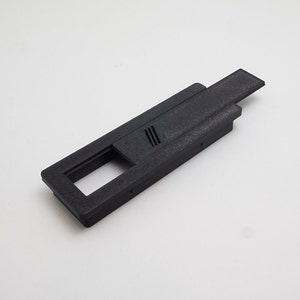 May include: Black plastic cable management box with a sliding cover. The box has a rectangular opening and a series of small holes for cable routing.