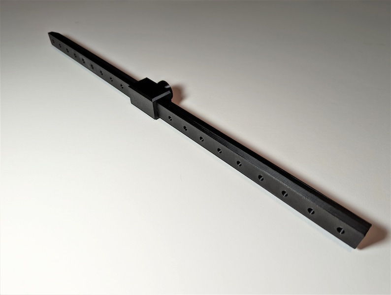 May include: A black metal tool with a rectangular body and a series of evenly spaced holes. A connecting piece with a knob is attached to the body. The tool is designed for precision and measurement.