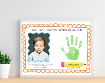 May include: A rectangular sign with an orange scalloped border featuring the text MY FIRST DAY OF KINDERGARTEN. It includes a photograph of a child, a green handprint, and a yellow pencil graphic with the name CHARLIE SMITH and August 15, 2026.