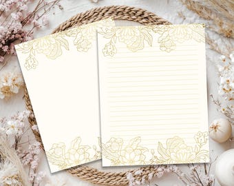 May include: Two sheets of off-white stationery paper featuring delicate gold-colored floral line art illustrations at the top and bottom borders. One sheet is blank, while the other sheet contains thin, horizontal gold-colored writing lines.