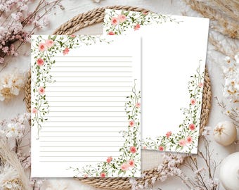 May include: Two sheets of white stationery paper featuring a watercolor illustration of climbing vines with pink roses and green leaves. One sheet contains horizontal black lines for writing, while the other sheet is blank with a floral border design.