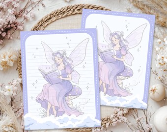May include: Two rectangular stationery sheets featuring a lavender and white illustration of a fairy with wings sitting on a mushroom while reading a book. The design includes a dashed border, soft clouds at the bottom, and small star accents.
