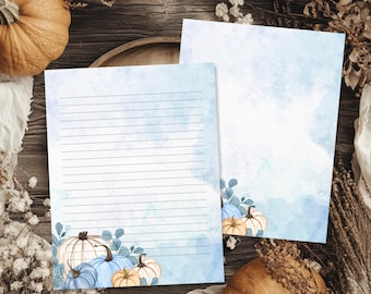 May include: Two rectangular sheets of stationery paper featuring a light blue watercolor wash background. The bottom corners are decorated with illustrations of pumpkins in shades of blue, cream, and orange, accented by green eucalyptus leaves.