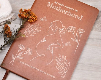 May include: A brown leather-textured journal with white line art featuring a pregnant figure, floral motifs, and the text "MY FIRST JOURNEY TO MOTHERHOOD" and "A LOVE STORY WRITTEN BEFORE WE MEET" printed on the front cover.
