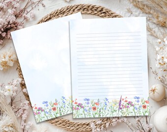 May include: Two sheets of stationery paper featuring a watercolor illustration of a wildflower meadow at the bottom. One sheet is blank, while the other contains horizontal lines for writing. The flowers include red poppies and blue cornflowers.