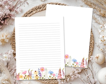 May include: Two sheets of white stationery paper featuring a colorful illustration of various wildflowers along the bottom edge. One sheet contains horizontal black lines for writing, while the other sheet is blank, both showcasing pink, blue, and yellow floral designs.