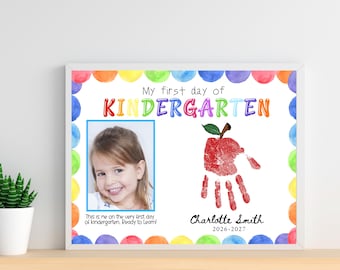 May include: A rectangular framed print featuring a colorful watercolor dot border. The text reads My first day of KINDERGARTEN. It includes a photograph of a child, a red handprint shaped like an apple, and the name Charlotte Smith 2026-2027.