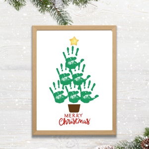 May include: A framed print featuring a Christmas tree design made of green handprints, topped with a gold star. The words "MERRY Christmas" are written in red script below the tree. The frame is a light brown color.