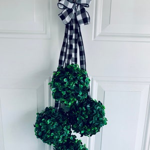 May include: A black and white checkered ribbon bow hangs from a door handle with three green topiary balls hanging below.