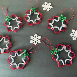 May include: Christmas ornaments in a snowflake design. The ornaments are made of red and silver pipe cleaners, with a green accent and a red loop for hanging. Two white snowflake cutouts are also present.
