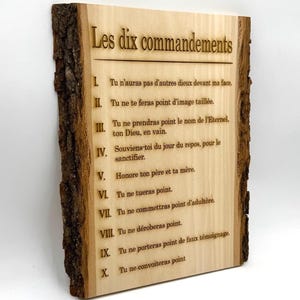 May include: A wooden sign with the Ten Commandments written in French. The sign is made of a natural wood slice with the bark still attached. The text is engraved into the wood.