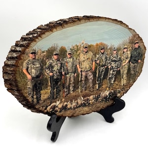 May include: A round wooden slice with a printed image of a group of people wearing camouflage clothing and holding rifles. The image is set in a wooded area with a blue sky in the background. The wooden slice is on a black stand.