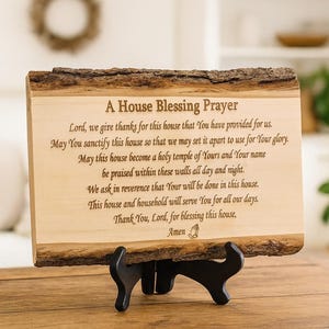 Könnte beinhalten: Holztafel mit natürlichem Rindenrand, die ein Gebet mit dem Titel "A House Blessing Prayer" zeigt. Die Tafel wird von einem schwarzen Ständer getragen. Der Text ist in einer klassischen Schrift graviert.