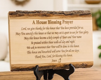 May include: A wooden plaque with a natural bark edge, displaying a prayer titled "A House Blessing Prayer." The plaque is supported by a black stand. The text is engraved in a classic font.