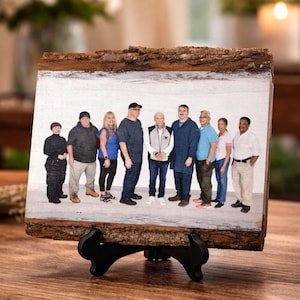 May include: A wooden block with a family portrait, supported by a black stand. The image features a group of people standing together. The wood has a natural bark edge, adding a rustic touch to the display.