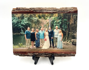 May include: A rectangular wood slice plaque featuring a printed photograph of seven people standing in front of a waterfall and lush greenery. The natural bark edges are visible on the top and bottom, and the plaque rests on a black plastic stand.