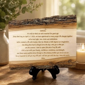 May include: A rectangular piece of natural wood with rough, dark bark edges on the top and bottom. The smooth, light-colored center surface features dark brown engraved text addressed to Gabriene, detailing a five-year wedding anniversary message.
