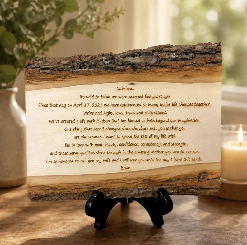 May include: A rectangular piece of natural wood with rough, dark bark edges on the top and bottom. The smooth, light-colored center surface features dark brown engraved text addressed to Gabriene, detailing a five-year wedding anniversary message.