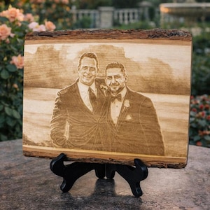 May include: A rectangular wooden plaque with natural bark edges featuring a laser-engraved portrait of two individuals wearing formal suits and bow ties. The plaque is displayed on a black plastic stand, showcasing a detailed wood-burned image.