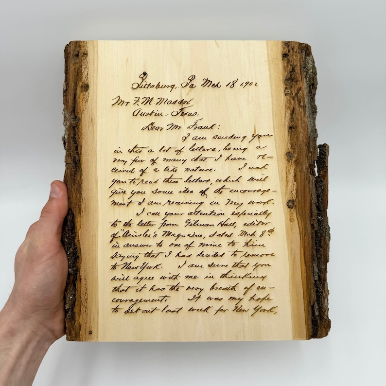 May include: A rectangular piece of light-colored wood with natural bark edges on the left and right sides. The surface features a dark, laser-engraved reproduction of a handwritten letter dated March 18, 1902, addressed to Mr. F.M. Massol.