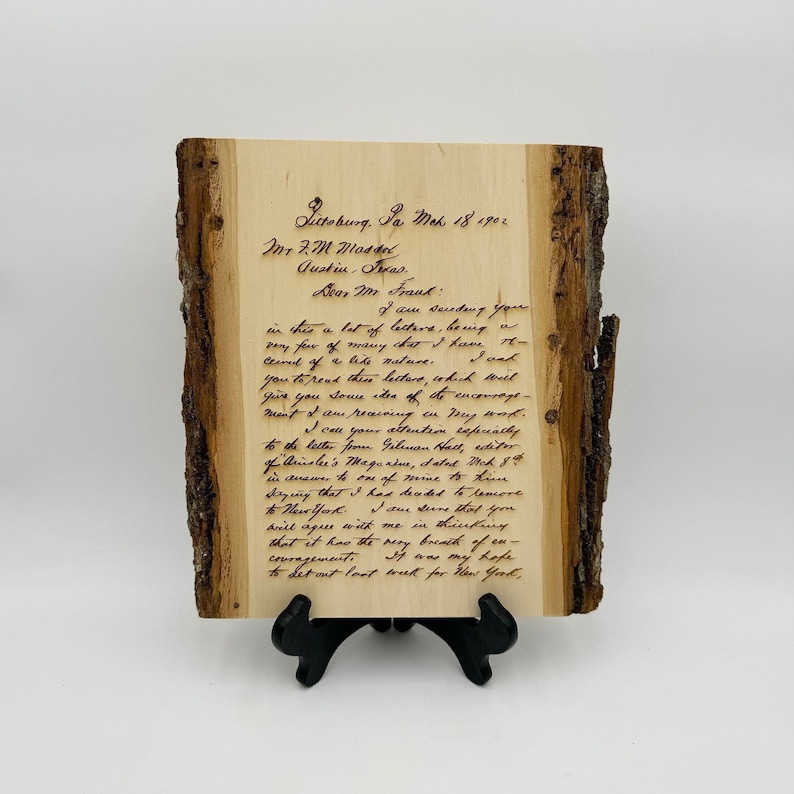 May include: A rectangular piece of light-colored wood with natural bark edges on the sides, featuring a dark, laser-engraved reproduction of a handwritten letter dated March 18, 1902, addressed to Mr. F.M. Mossel in Austin, Texas, resting on a black stand.